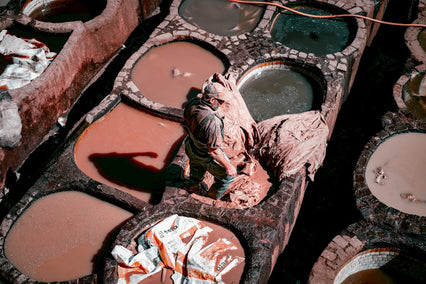 Worker processing leather in an ancient tannery with colorful vats, showcasing traditional methods.