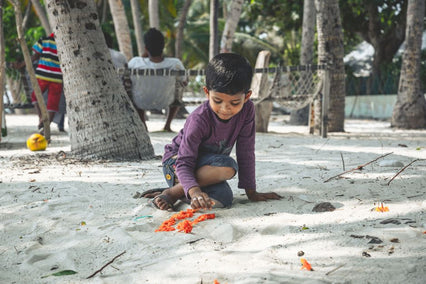 A young boy playing with sand on a sunny tropical beach in Maalhos, Maldives.