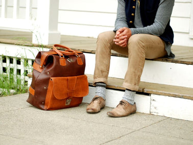 A person sitting on a porch with a vintage leather bag nearby, showcasing casual style.